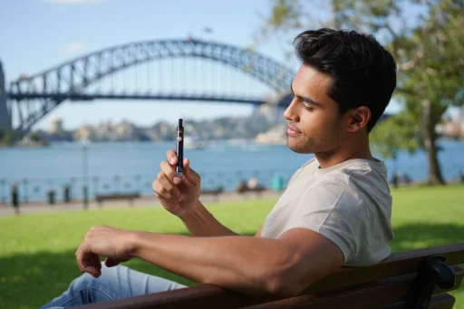 A person in a casual Australian urban setting, like a park in Sydney, thoughtfully examining a sleek pod vape they recently chose to buy vapes online.